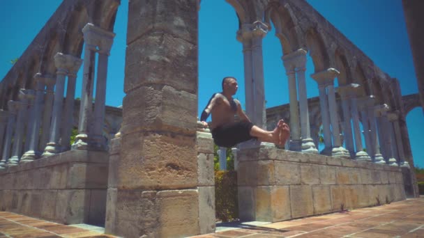 Sportler schüttelt den Bauch und zieht die Beine zwischen den antiken Säulen hoch — Stockvideo