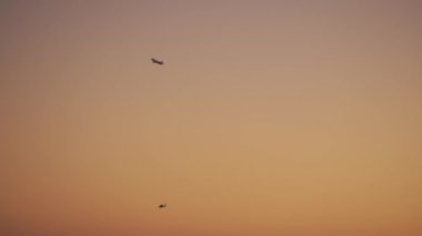 Uçak ve helikopter gün batımında turuncu gökyüzünde farklı yollarda uçar.