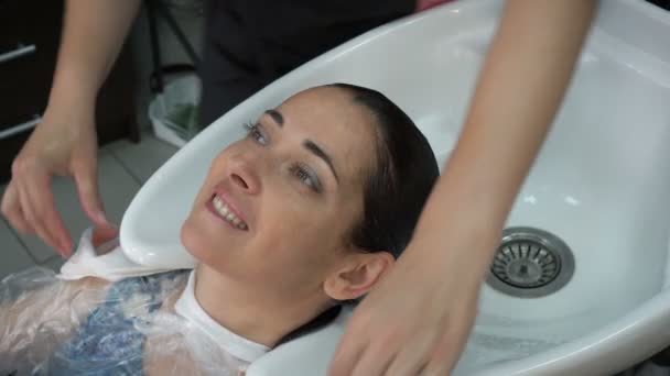 发型师洗完头 用毛巾裹着头 从水里挤出黑发女孩的头发 女孩看着相机 微笑着 高细节 25Fps — 图库视频影像