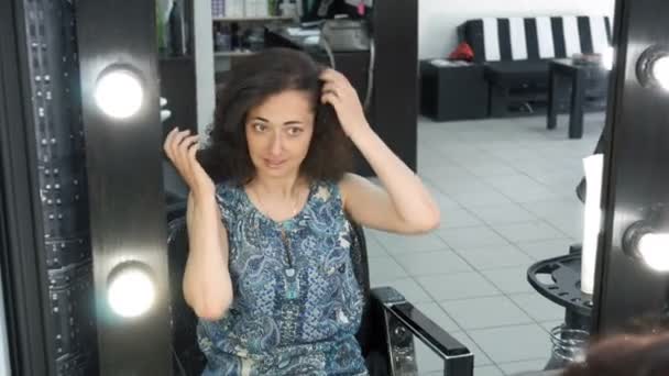 美しいヘアスタイルを持つ女性は 美容院の鏡の前に座っている自分を賞賛します 彼女の髪を整えたり 鏡の中に見えます 重要なイベントを準備している女の子 — ストック動画