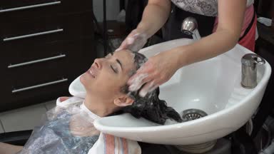 Berber Kuaför dükkanı lavaboda üzerinde esmer kızın saçları şampuanla sabunlar ve kafasını masajlar. Kız gülümsüyor ve Kuaför konuşur. Yakın çekim, yüksek detay. 4k, 25fps