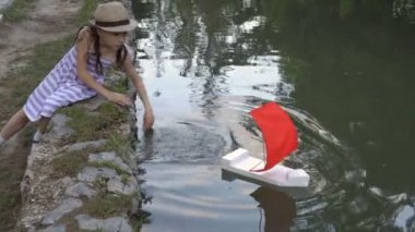 Mutlu küçük kız şehir Park Su birikintisi tarafından yaz aylarında oynar ve beyaz bir oyuncak ile kırmızı bir yelkenli gemi su içine başlattı. Yüksek detay. 4k, 25 fps