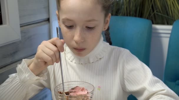 カフェに座っていると ピンクのアイスクリームを食べる彼女の顔にそばかすのある思いやりのある女の子 彼女が周りに見えるし 笑顔します クローズ アップ顔 ハイディテール Fps — ストック動画