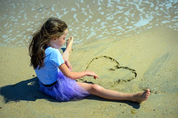 보라색에 화창한 날에는 해변에 모래에 복장과 모래에 그녀의 손으로 마음을 — 스톡 사진