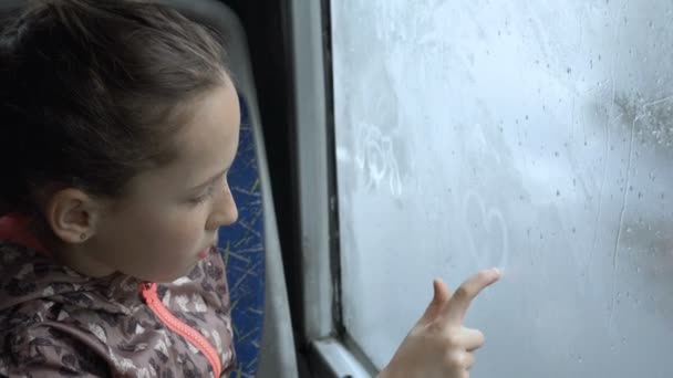 一个小女孩用手指在公共汽车上的湿迷离玻璃上画出她的心 关门了高细节 Fps — 图库视频影像
