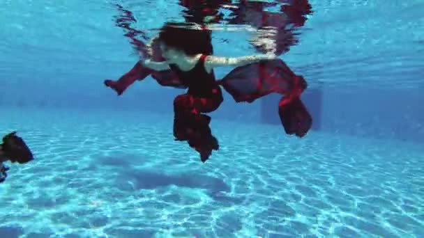 一名男子摄影师采取一个专业的水下相机美丽的女孩新娘红头发 谁游泳水下在泳池中的红色礼服 慢动作 Fps — 图库视频影像