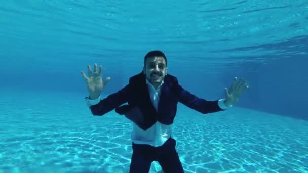 一个穿着蓝色西装 白衬衫的男人在水池里游泳 在水下摆姿势 他看着相机 挥动着双手 微笑着 射击行动照相机在水下 Fps — 图库视频影像