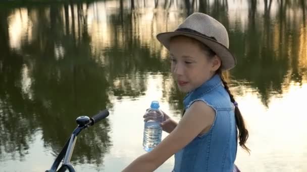 Счастливая Маленькая Девочка Велосипедом Смотрит Камеру Улыбается Берегу Реки Закате — стоковое видео
