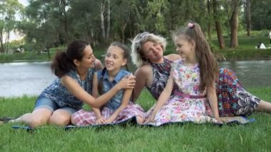 Mutlu eşcinsel aile: iki anne ve iki kızı, oturup, oyun ve nehrin yanında Park'ın bahçesinde günbatımında gülüyor. 4 k. 29,97 fps.