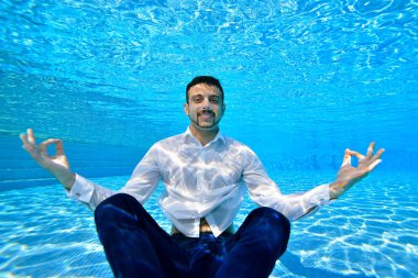 Beyaz gömlekli, sakallı, Genç bir oryantal adam havuzunda sualtı Lotus pozisyonu dibinde oturur ve kameraya benziyor. Yakın çekim. Sualtı fotoğrafçılığı. Yatay yönlendirme.