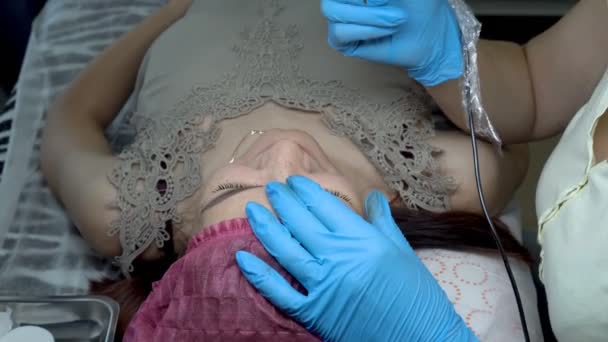 一个年轻女孩在美容院做永久性化妆眉毛 美容师用针把黑漆涂在眉毛上 Microblading 关门了从顶部的视图 Fps — 图库视频影像