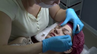 Kadın güzellik uzmanı bir güzellik salonu microblading yordamda sonra genç bir kızın kaşları krem smear. Kalıcı makyaj kaşlar. Yakın çekim. Üstten görünüm. 4k, 25 fps.