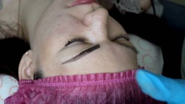 Güzellik uzmanı kalıcı makyaj yapar ve bir kız bir güzellik salonu içinde kaşları bir iğne ile siyah boya uygulayabilirsiniz. Microblading yordam. Üstten görünüm. Son derece yakın çekim. 4 k. 25 fps.
