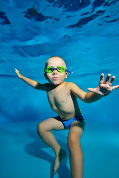 A little boy swims and plays under the water at the bottom of the pool with green swimming glasses. Portrait. Vertical orientation.