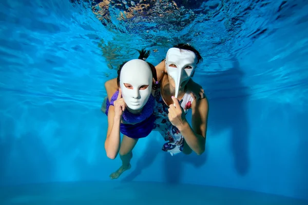 一个孩子和一个穿着白色化装面具的母亲在泳池里的水里游泳 摆出漂亮的连衣裙 看着摄影机 戏剧表演 图像的水平方向 — 图库照片