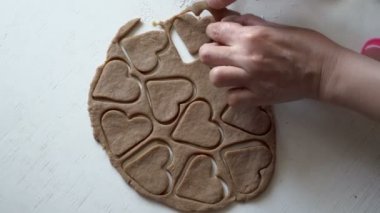 Bayan Baker tanımlama bilgileri hazırlar. Haddelenmiş kahverengi hamur ürünleri beyaz bir tablo üzerinde kalp şeklinde bir heykelcik dışarı keser. Yakın çekim, yüksek detay. Üstten görünüm. 4 k. 25 fps.
