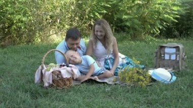 Mutlu bir aile: Baba, anne ve küçük bir çocuk parkta piknik vardı. Onlar oynamak ve çim üzerinde oturan gülümse. 4 k. 25 fps.