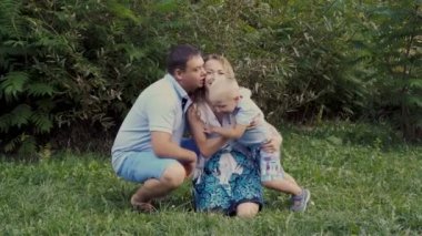 Anne, baba ve eğleniyor ve çim yeşil bir arka plan üzerinde parkta oynarken küçük oğlu. Gülmek, sarılmak ve öpmek. Vintage işleme. 4 k. 25 fps.