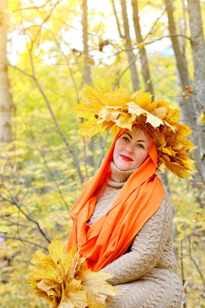 The blonde girl is a large size in a wreath of autumn leaves sitting and smiling in the forest on a yellow background. Size plus and xxl woman. Portrait. Vertical view.