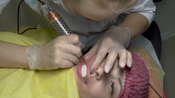 Zabieg kosmetyczny Makijaż permanentny ust. Kobieta kosmetyczka stosuje farby z igłą w usta dziewczyny, w salonie piękności. Z bliska. Widok z góry. 4 k. 25 fps. — Wideo stockowe