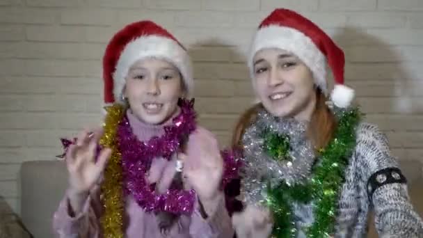 Portrait of two happy cheerful children who sit in Santas hats with Christmas tinsel on their shoulders. They dance, laugh, move to the music and look at the camera. Close up. 4K. 25 fps — Stock Video