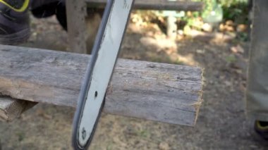Bir adam bir chainsaw eski ahşap tahta açık havada karşı ayağı ile dinlenme güneşli bir testere. Yakın çekim. Üstten görünüm. 4 k. 25 fps