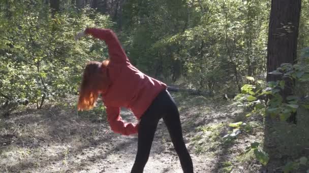 公園でスポーツをしている赤い髪の少女 彼女は赤いジャケットに晴れた日にクリアで体操を行います リアビュー クローズ アップ Fps — ストック動画