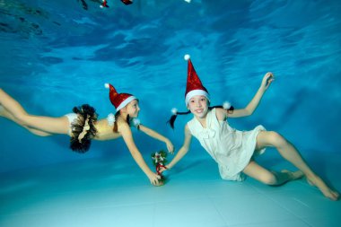 Noel Baba'nın kırmızı şapka çocuklarda sualtı dalış havuzun dibinde, mavi bir arka plan üzerinde küçük bir Noel ağacı ile oynamak, kamera ve gülümseme bak. Portre. Sualtı çekim.
