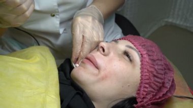 Bir kadın güzellik güzellik salonu kalıcı makyaj dudaklarında prosedürü sırasında genç bir kızın üst dudak üzerinde bir iğne boya hıyarlar. Portre. Yakın çekim. Üstten görünüm. 4 k. 25 fps.