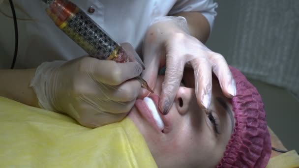 特写镜头 一个女人在嘴唇上做纹身 她躺在沙发上 医生美容师用针头和油漆治疗她的嘴唇 永久唇妆 从顶部的视图 — 图库视频影像
