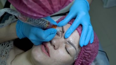 Güzellik uzmanı Doktor kalıcı makyaj kaşları kız güzellik salonunda yapar ve siyah boya kaşlarını üzerinde neden olur. Microblading yordam. Yakın çekim. Üstten görünüm. 4 k. 25 fps.