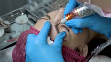 Yakın çekim yordamı microblading kaşlar. Ana Şevval özçelik güzellik kızın kaş ile bir pamuklu çubukla losyonları ve siyah boya bir iğne ile bıçakladı. Kalıcı makyaj kaşları güzellik salonu içinde. 4 k. 25 fp