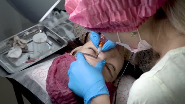 女の子美容サロン マスターの美容師が彼女の眉毛黒の塗料の針です ビューティー サロンでアートメイク眉 クローズ アップ手順 Microblading Fps — ストック動画