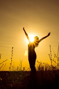 A young happy girl stands with open arms against the sun rays on the top of the mountain among the plants. Vertical orientation of the image. clipart