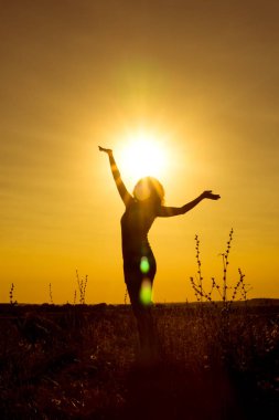 Happy and free girl stands with arms outstretched in the background of the yellow sunset on top of the mountain among the plants in the bright rays of the sun. Silhouette. Concept. Vertical view. clipart