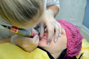 Kalıcı dudak makyaj güzellik salonu kız yordamı Close-up. Şevval özçelik güzellik bir iğne boya dudaktan hıyarlar. Üstten görünüm. Resmin yatay yönünü.