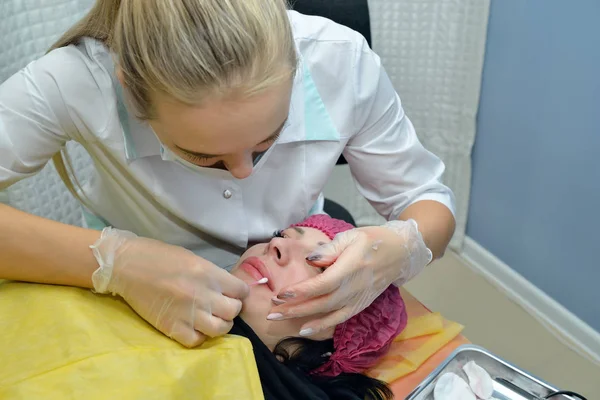 Cosmetologist-the doctor treats lips to the woman at the beauty salon and lubricate her lips with ointment after the procedure of permanent lip makeup. Portrait. Close up. Horizontal view.