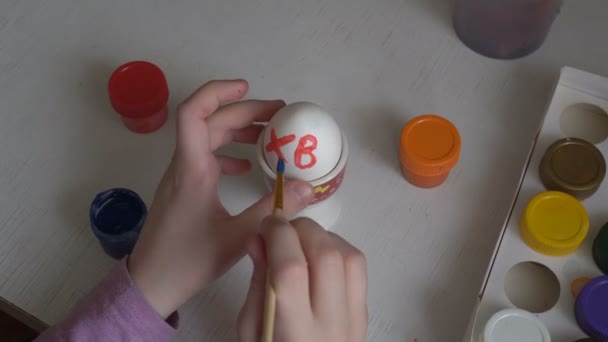 El niño pinta los colores del huevo de Pascua y dibuja símbolos en él con un pincel. De cerca. La vista desde arriba. 4K. 25 fps — Vídeo de stock