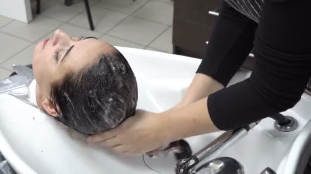 Perawatan rambut. Penata rambut mencuci kepala gadis-gadis setelah potongan rambut di toko Barber di atas sampo washbasin putih. Tutup. 4K. 25 fps — Stok Video