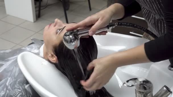 The Barber washes the head of a beautiful Oriental girl in a Barber shop over a white washbasin. Hair care. Close up. The view from the top. 4K. 25 fps — Stock Video