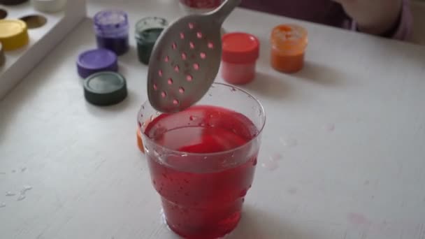 La famille s'assoit à la table et peint l'œuf dans un verre avec de la peinture rouge. Préparation pour Pâques. Ferme là. 4K. 25 ips — Video