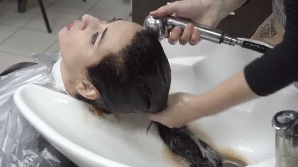 Kadeřník omývá hnědé barvy z vlasů dívky v holičství po stříhání a postupy barvení vlasů. Péče o vlasy. Zblízka. 4 k. 25 snímků / s — Stock video
