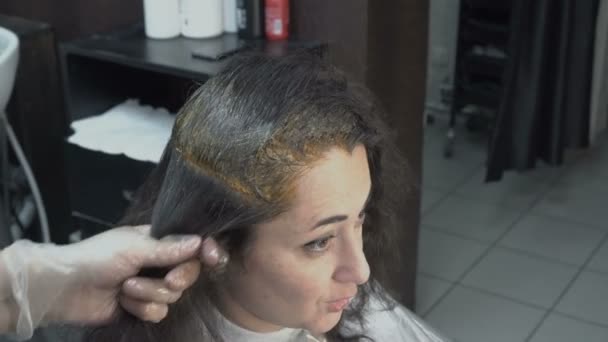 Frisör-stylist sätter måla på enskilda delar av hår flicka som sitter framför en spegel i salongen-skönhet. Hår vård. Närbild. Utsikten från toppen. 4k. 25 fps. — Stockvideo