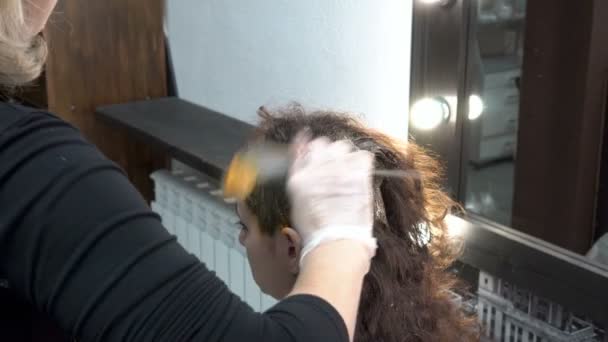 En kvinna frisör målar en flickas hår i en frisersalong och sätter färg på huvudet med en borste. Hårvård. Närbild. 4 k. 25 fps. — Stockvideo