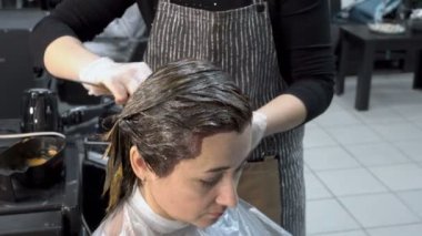Kuaför dükkanında saç boyama. Berber dükkanında oturan yetişkin bir kız, ve Kuaför saçını boya koyar. Saç Bakımı. Kapat şunu. 4k. 25 fps.