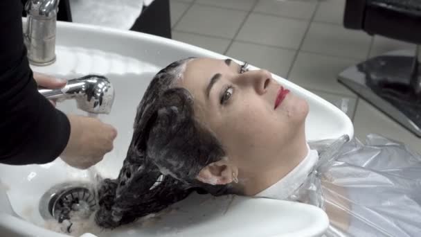 女性美容師は、美容サロンで東洋の女の子の頭を洗います。髪のケア。クローズ アップ。4 k. 25 fps. — ストック動画