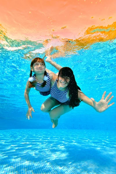 Mamá enseña a su hija a nadar en la piscina. Nadan y juegan bajo el agua con trajes de baño a rayas sobre un fondo de rayos de sol. Retrato. Disparando bajo el agua. Orientación vertical — Foto de Stock