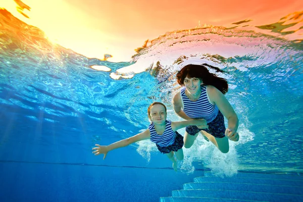 Familia feliz, madre e hija, practicar deportes de vacaciones y nadar bajo el agua en la piscina en trajes de baño a rayas en un día soleado brillante. Miran a la cámara y sonríen. Retrato. Vista inferior — Foto de Stock