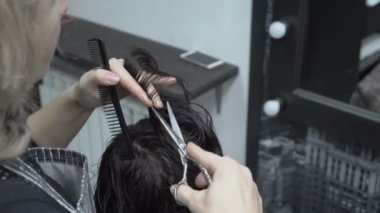 Kuaför stilist tarak ve berber dükkanı aynanın önünde oturur makas ıslak saç kız keser. Saç Bakımı. Yakın çekim. Arka yan görünüm. 4 k. 25 fps.