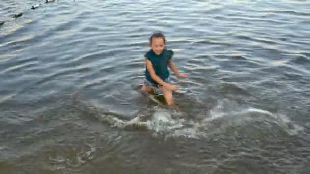Vrolijke jonge meisje spelen in het water bij zonsondergang. Ze spuit water aan de zijkanten met haar handen en lacht. Het uitzicht vanaf de top. 4k. 25 fps. — Stockvideo